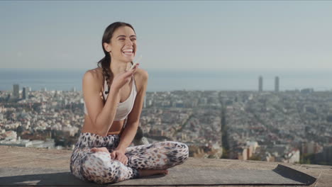 mujer de yoga grabando un mensaje de voz en un teléfono inteligente contra la vista de la ciudad de barcelona