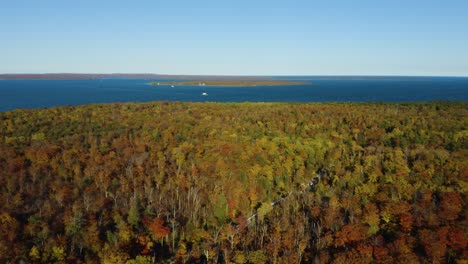 Drone-Flies-High-Above-Colorful-Autumn-Forest-with-Lake-on-Horizon