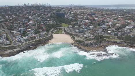 Vista-Aérea-De-La-Playa-De-Tamarama-Y-El-Mar-Azul-Con-Olas---Edificios-En-Bondi,-Tamarama-Y-Bronte-En-Los-Suburbios-Del-Este-De-Sydney,-Nsw,-Australia