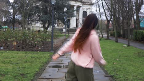 long haired stylish female urban dancing on park pavement towards white building with columns