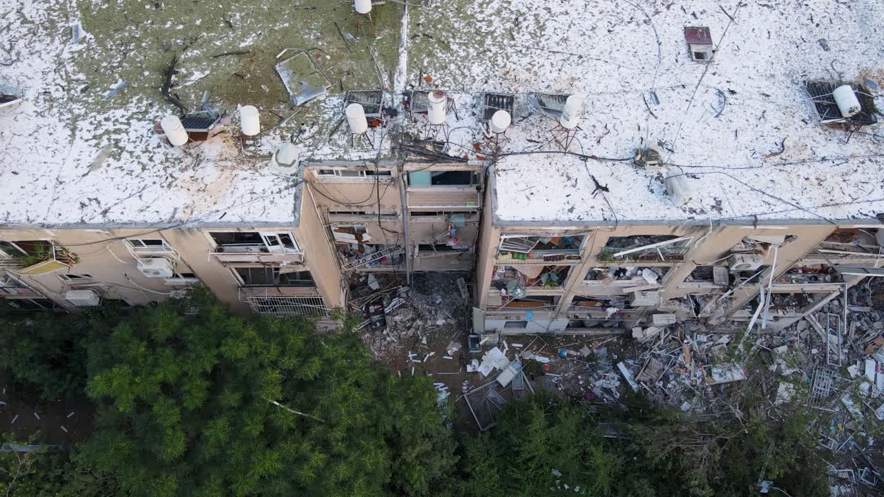 Aerial top-down view of a damaged residential building in northern Tel Aviv. building shows heavy structural destruction following an Iranian missile strike, with all windows shattered and debris