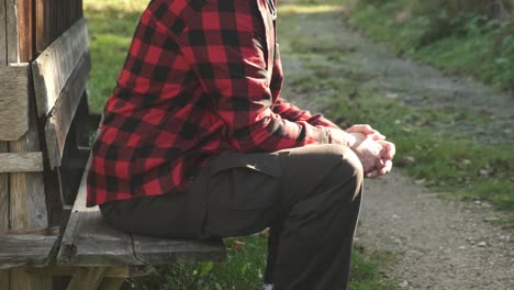 Hombre-Con-Una-Camisa-De-Cuadros-Roja-Sentado-En-Un-Banco-Exterior-Pensando-En-Detalles