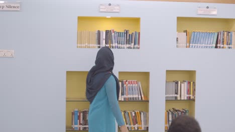 woman in hijab browsing bookshelves in a library