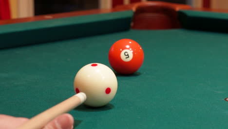 closeup of person playing pool shooting solid orange 5 ball into corner pocket after practice strokes using cue ball with red spots, open bridge hand with wooden cue stick and green felt or cloth