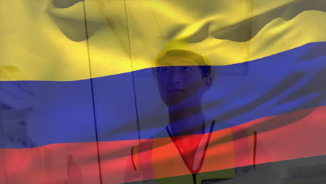 Animación-De-La-Bandera-De-Colombia-Ondeando-Sobre-Un-Sonriente-Arquitecto-Asiático-Con-Casco-Sosteniendo-Un-Plano