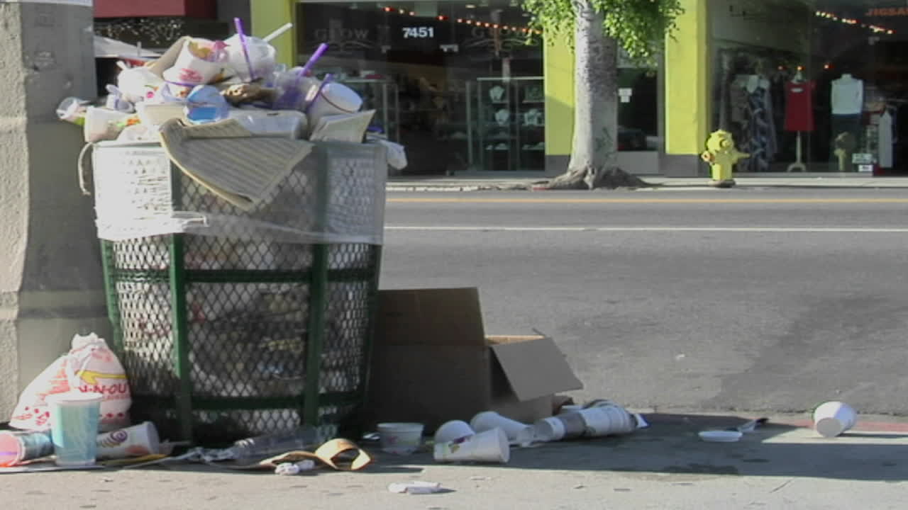 Trash spills out of an overfilled trash can on a city street