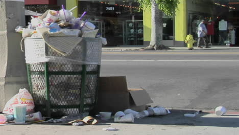 trash spills out of an overfilled trash can on a city street