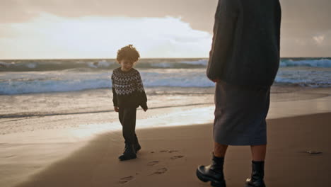 kid mother walking sand beach leaving footprints on sunset. joyful family play