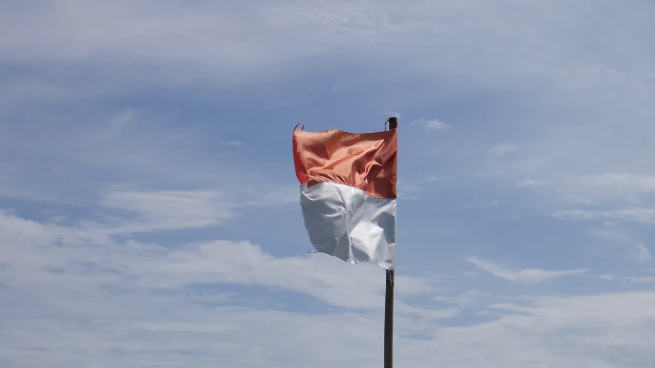 Bandiera indonesiana che sventola sull'asta della bandiera sullo sfondo del cielo blu