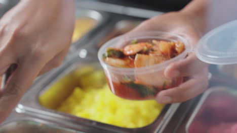 placing kimchi in a round plastic food container for takeaway