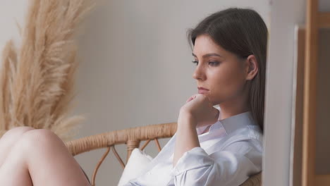 Sad-thoughtful-lady-sits-in-rattan-armchair-in-studio