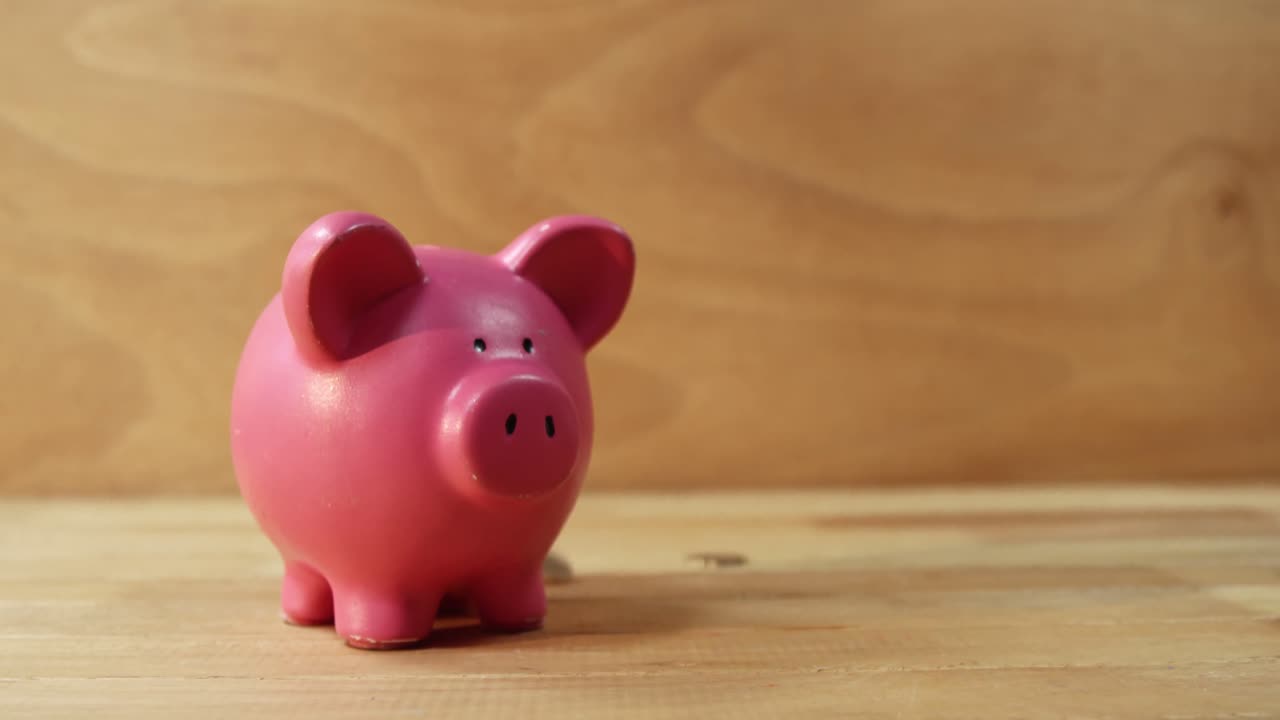 monedas cayendo en la alcancía contra un fondo de madera