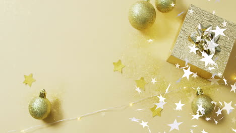 animation of stars over christmas present and baubles on yellow background