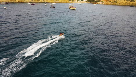 Couple-Jetskiing-In-The-Blue-Ocean-Passing-By-Anchored-Boats-In-Ibiza-Island,-Spain