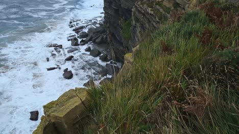 From-the-edge-of-the-cliff-of-the-Isla,-Cantabria,-one-can-seen-the-beautiful-Cantabrian-sea-hitting-the-shore-violently