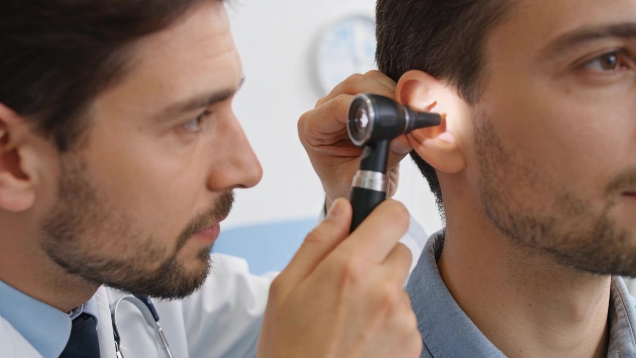 Dottore in camice bianco che esamina l'orecchio destro del paziente in clinica, usando un otoscopio per la diagnosi.