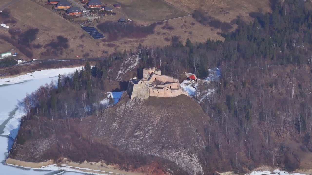 Luftfoto af et historisk slot med udsigt over en flod, omgivet af frodige skove og bjerge i det tidlige forår.