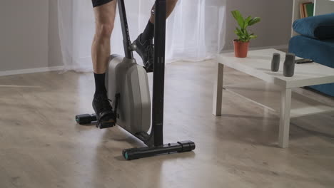 elderly man is spinning pedals of exercise bike training at home spinning pedals in his living room at weekend keeping fit and health closeup of legs and feet