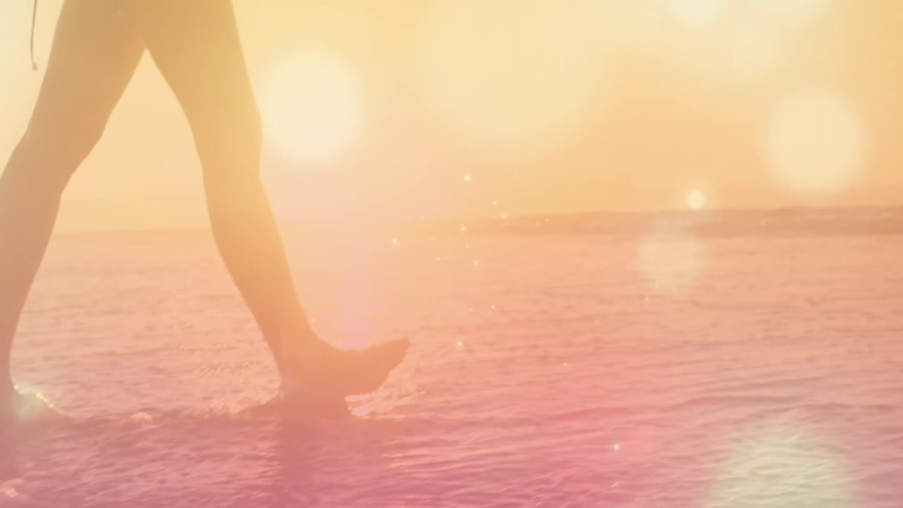 빛나는 반점이 들어오는 해변에서 걸어다니는 여성의 낮은 부분의 디지털 복합 비디오