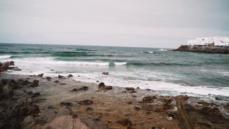 Panning-shot-of-stormy-waves-reaching-rocky-shore-of-Gran-Canaria-during-cloudy-sky-outdoors