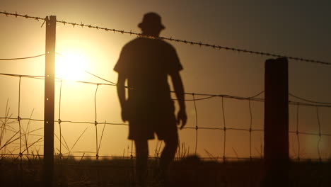 silhouette of farmer walking along and away from wire fence