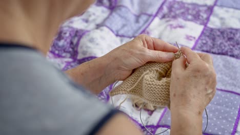 a close-up view from behind the back of the hand of an old grandmother who knits warm clothes for her relatives. hobby closeup knitting by old men. favorite pastime of retirees