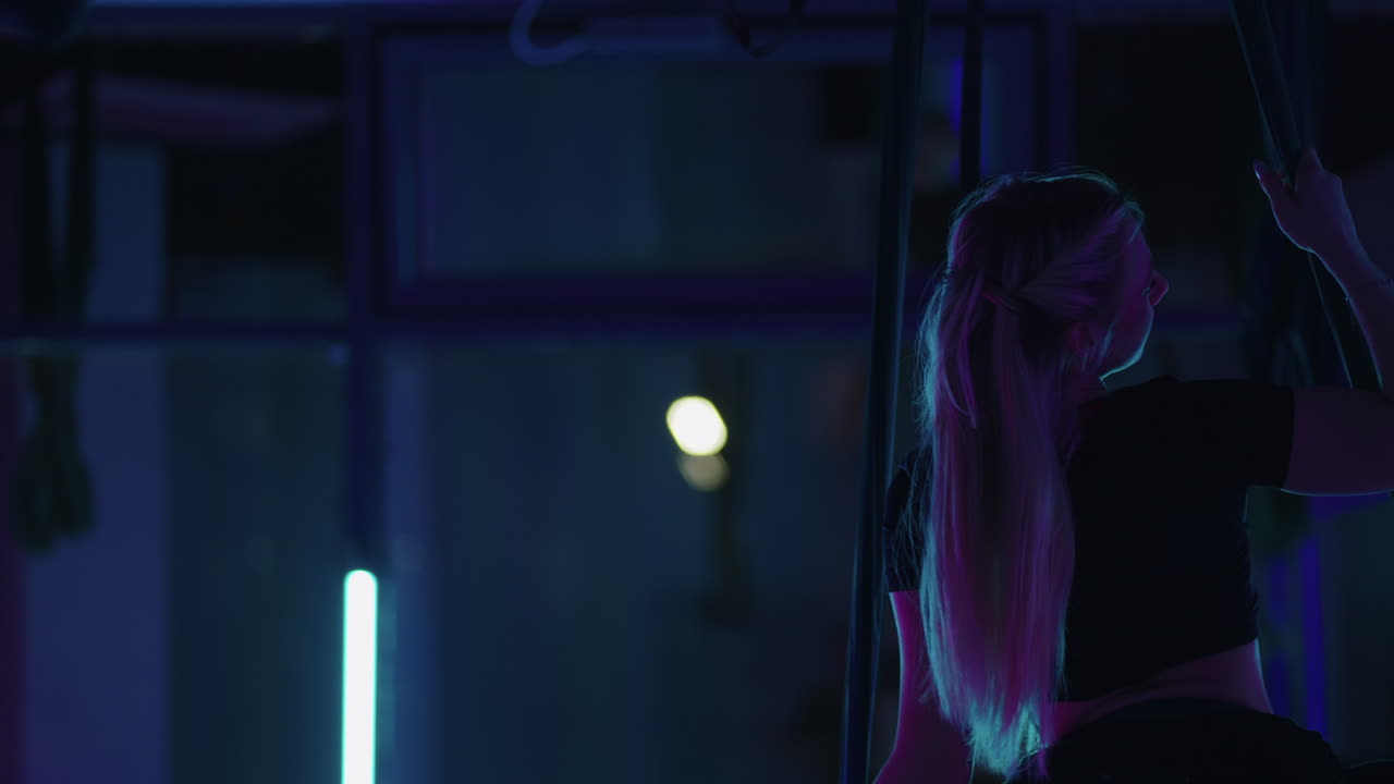 una graciosa y delgada dama está sentada en posición dividida en una hamaca para hacer yoga con mosca y moviéndose por encima del suelo