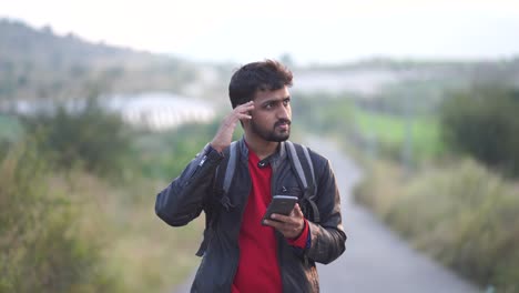 young man with beard, traveling in the mountains and looking at his mobile phone