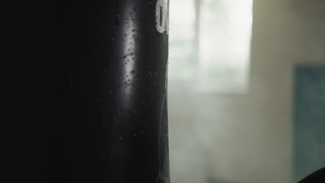 Professional athlete hand in sports glove hits punching bag releasing aggression and improving stamina in fight club. Water droplets flow from equipment upon impact