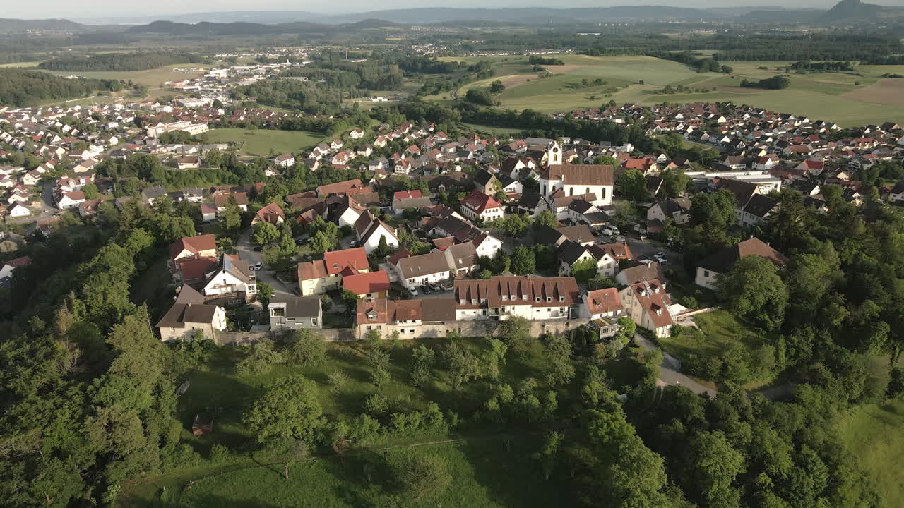 Drone footage moving forward from the opposite side, focusing on the historic town of Aach and its church tower, with a beautiful view of the surrounding landscape.
