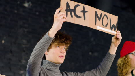 young environmental activist holding a cardboard with act now" inscription and protesting against climate change inaction"