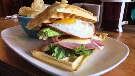 waffle sandwich with egg, bacon, avocado, ham and cheese with sidedish chips