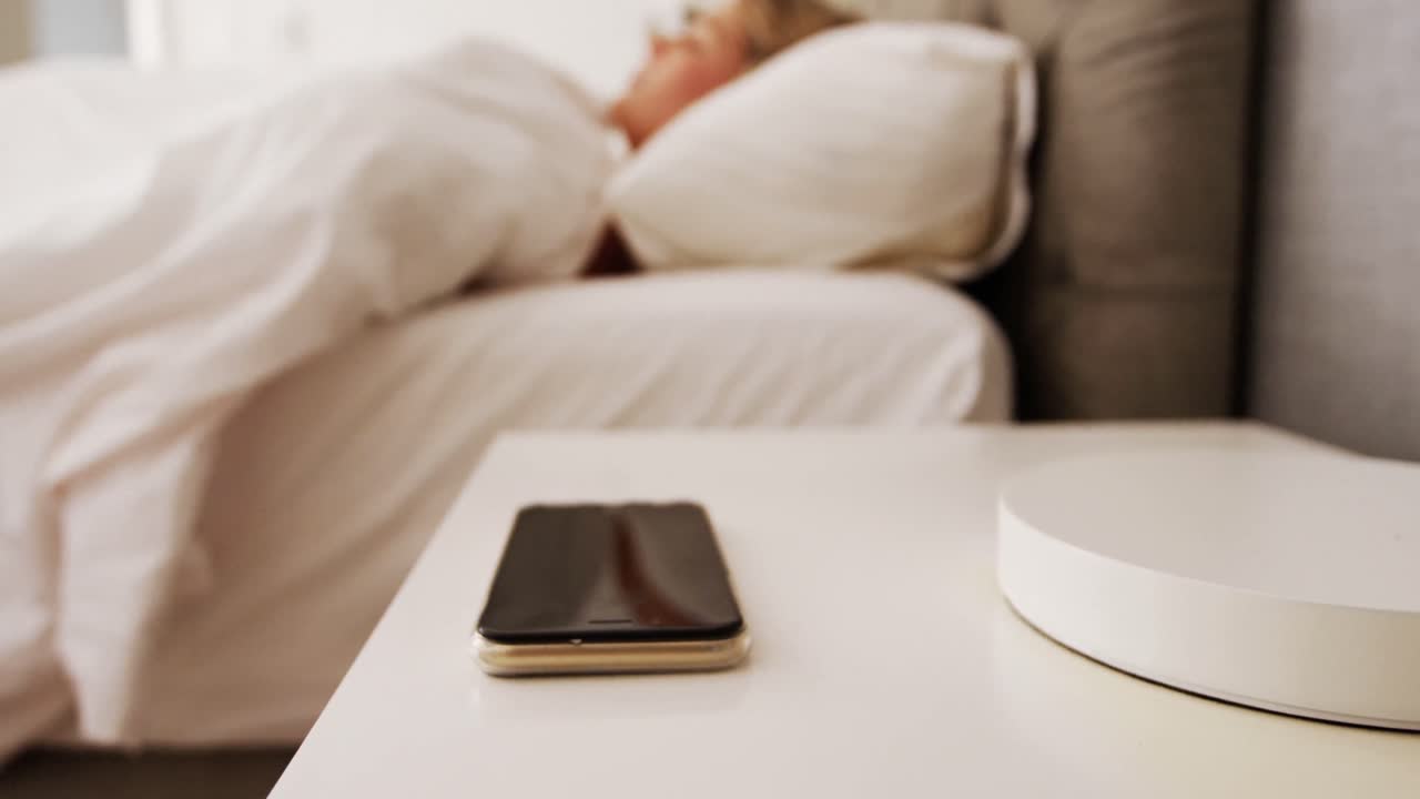 Woman sleeping on bed and picking up the phone from side table