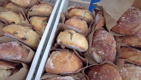 slow pan of loaves of fresh bread in paper bags ready to be sold at a local farmers market