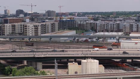 Traffic-in-Denver-city,-cars-on-motorway-and-train-passing-under-the-bridge