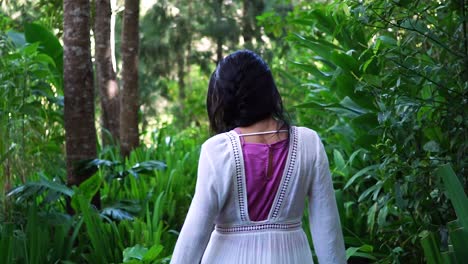 following a woman walking into the forest while touching and caressing the lush vegetation and the green leaves