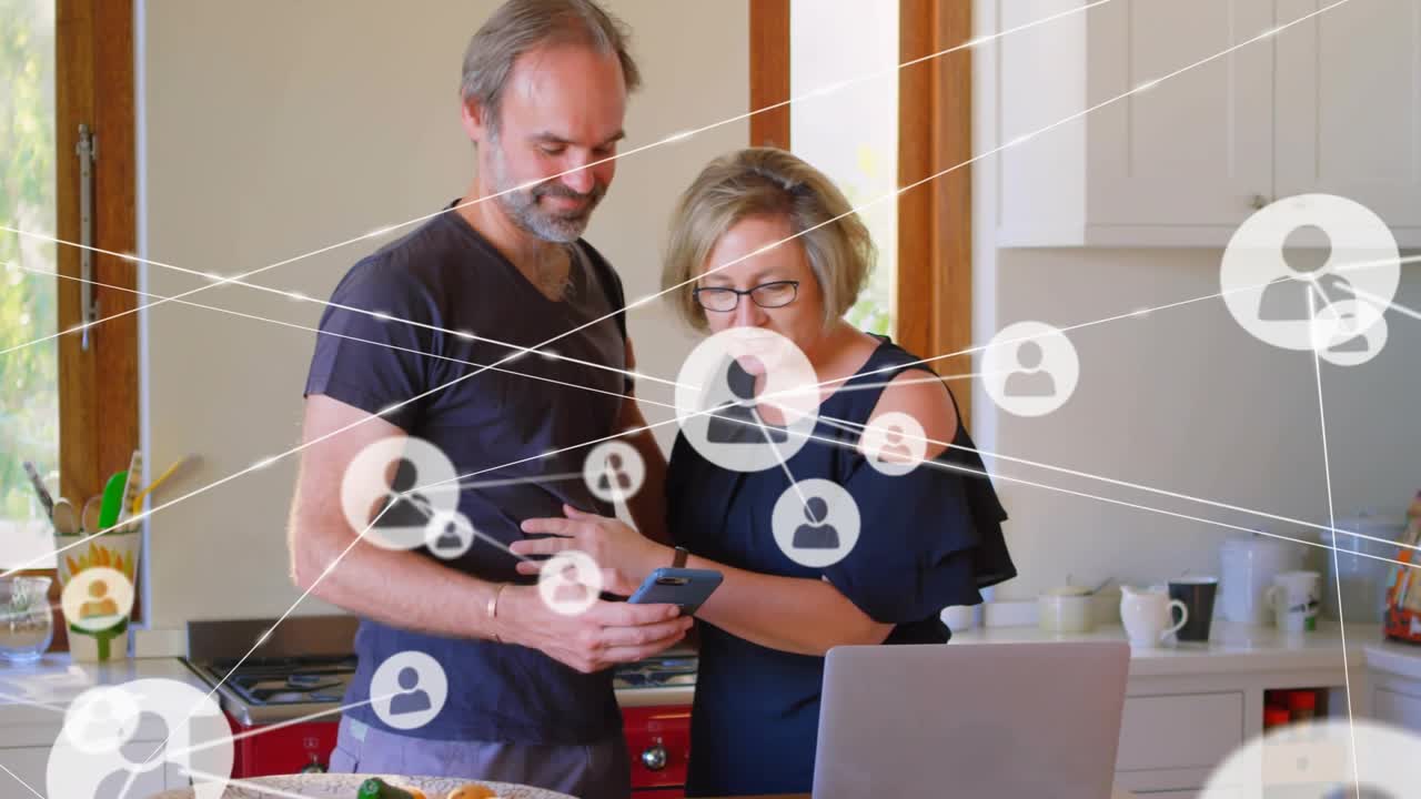 Couple hugging then scrolling phone in kitchen checking online data activating tech nodes on laptop