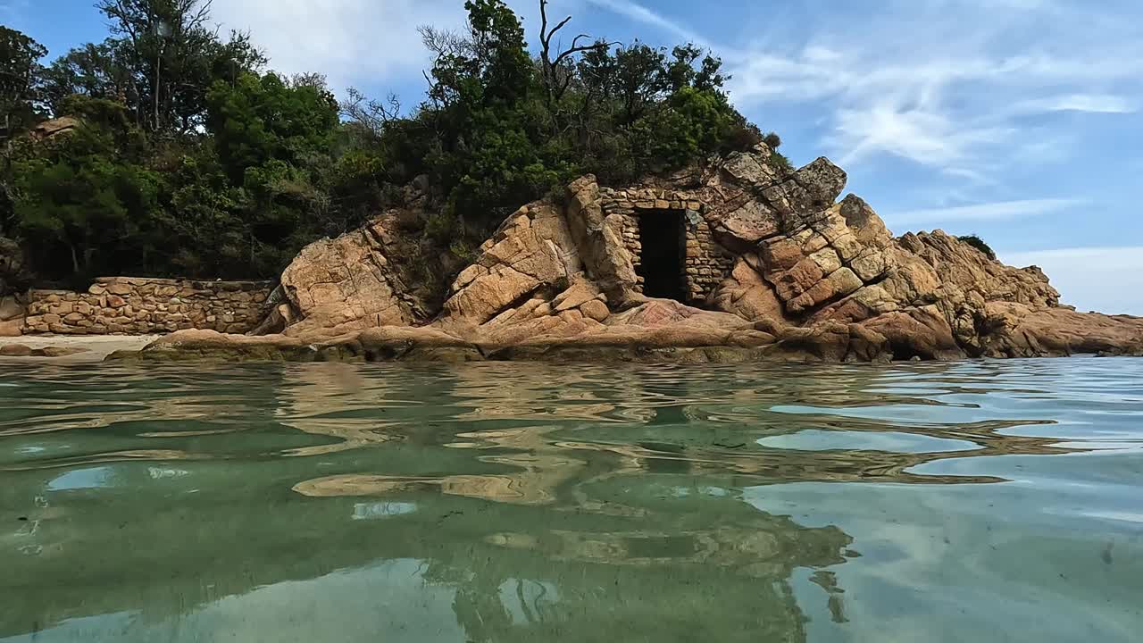 ángulo bajo de la superficie del agua pov de la antigua puerta de paso frente al mar tallada en la roca de la idílica playa de canella en la isla de córcega, francia
