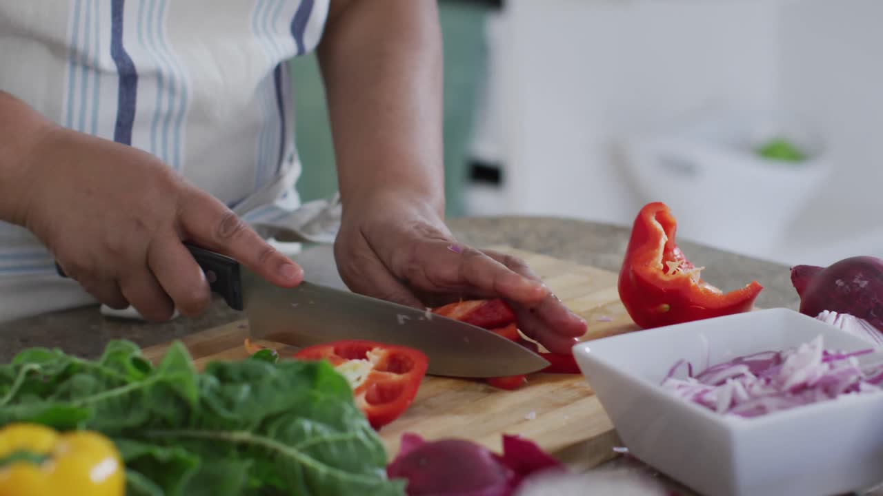sección media de una mujer mayor afroamericana preparando comida en la cocina, cortando pimienta roja