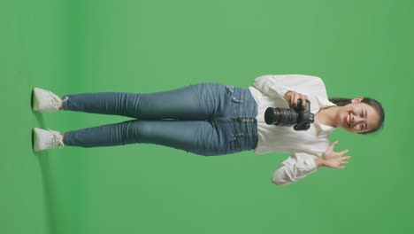 cuerpo lleno de fotógrafo asiático mirando las imágenes en la cámara y luego agitando la mano mientras estaba de pie en el fondo de la pantalla verde en el estudio