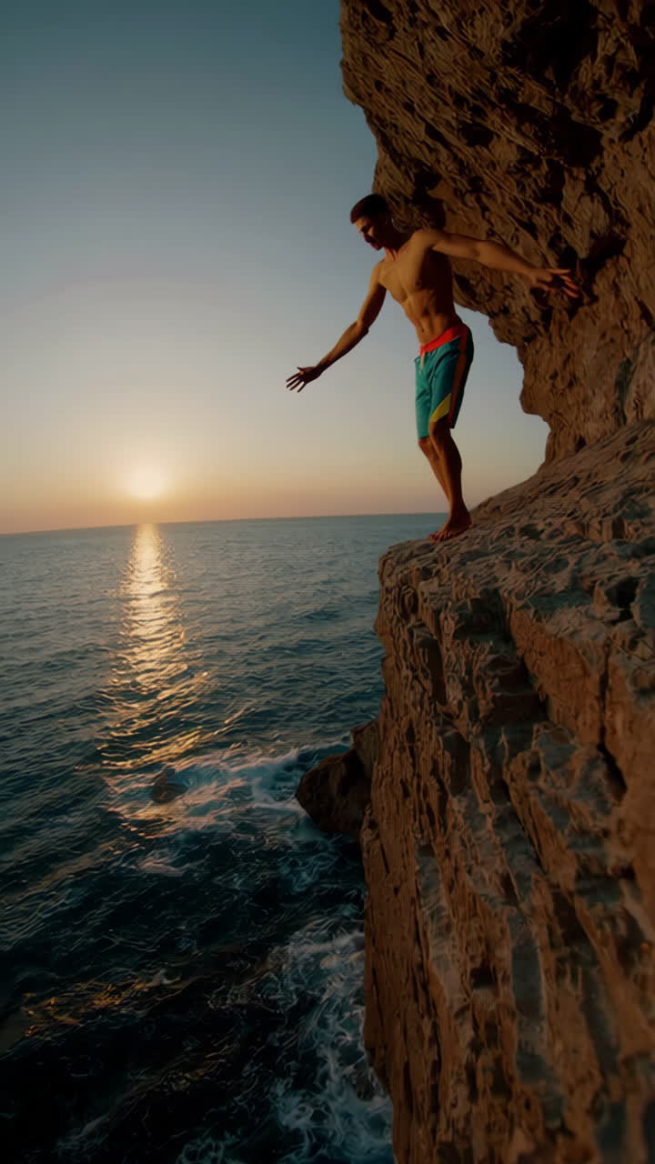 Man on a cliff edge contemplating a jump into the ocean at sunset