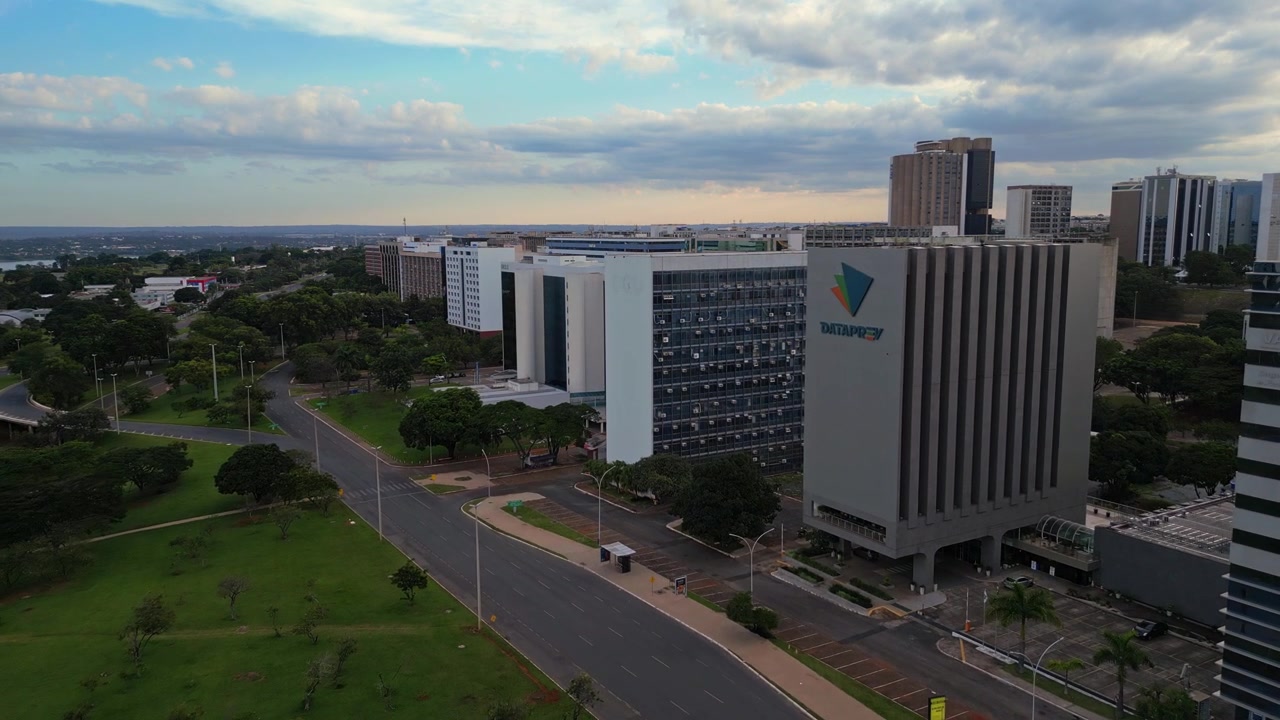 Vista aérea do edifício-sede da DATAPREV em Brasília, Brasil. A arquitetura moderna é cercada por áreas verdes, ruas e um céu nublado durante o dia.