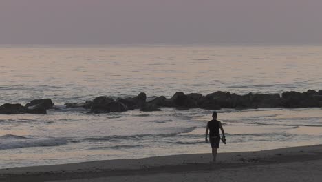 man walking on beach barefoot at dawn, slow motion silhouette