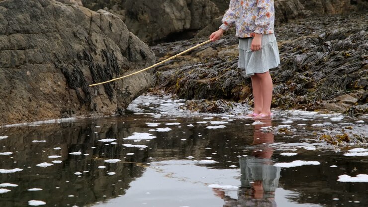 Young girl fishing in ocean pool on rocky coastline with her reflection in water