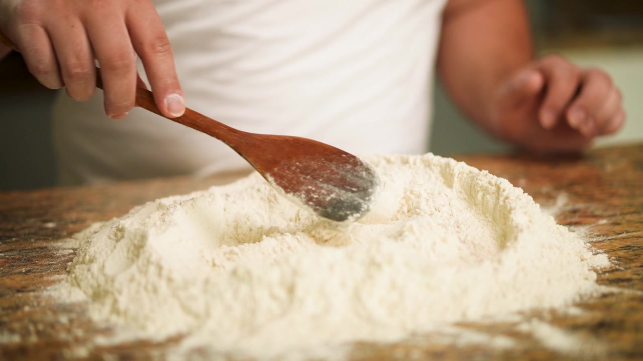 Un cuoco lavora la farina secca su un piano di lavoro, unendola per preparare l'impasto.