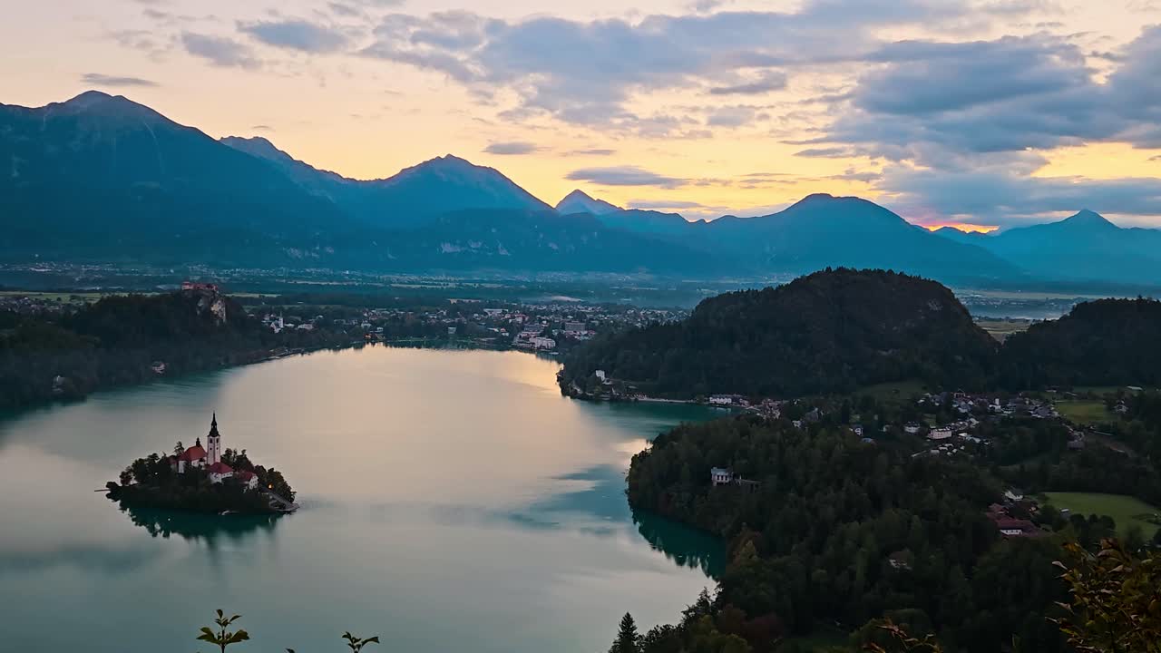 Luce dell'alba sul lago di Bled con acqua calma e montagne circostanti all'alba, carrellata orizzontale che inquadra la valle