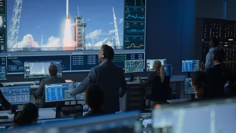 group of people in mission control center witness successful space rocket launch. flight control employees sit in front computer displays and monitor the crewed mission. team stand up and clap hands.