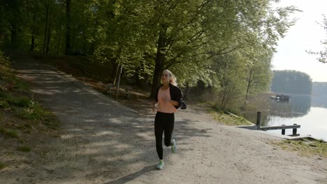 Woman-running-next-to-lake-and-woods-on-sunny-day