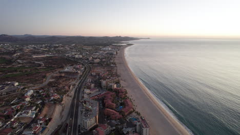 Coastal-highway-in-Los-Cabos,-Mexico-surrounded-by-resorts-and-hotels-in-a-calm-ocean-sunset
