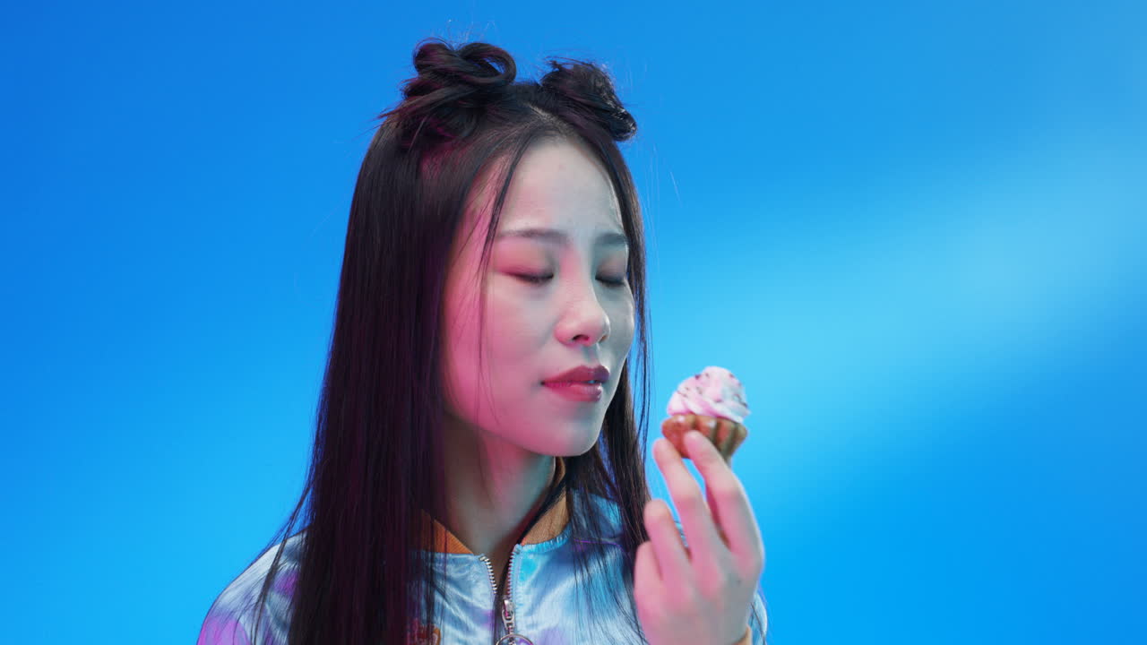 крупным планом женщина ест маленький кекс с розовым кремом